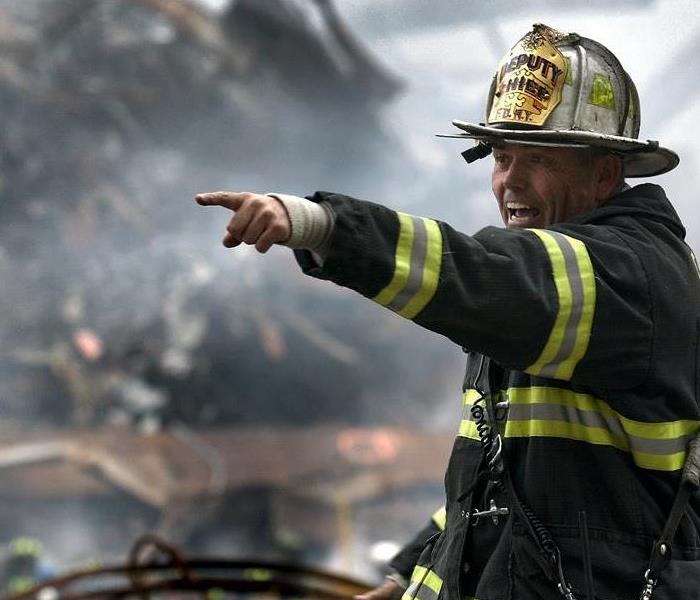 fireman pointing to the left and shouting with a pile of burning debris in the background
