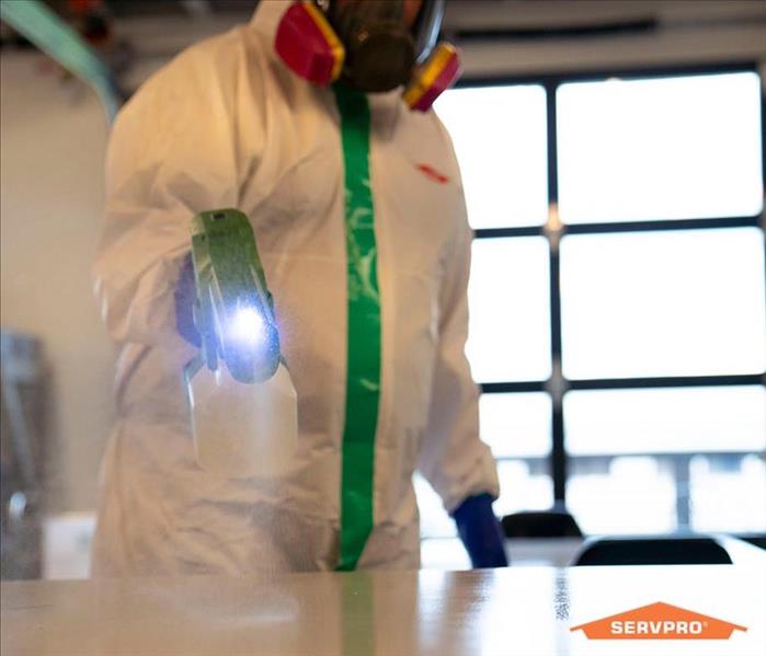 man in full PPE spraying disinfectant on a white countertop for COVID-19